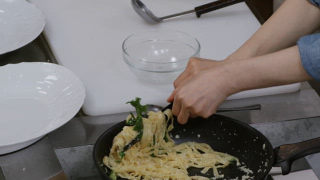 Person serving pasta onto a plate inside a kitchen