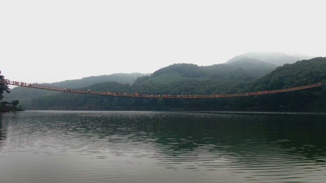 People walking on a suspension bridge over a lake with blue mountains