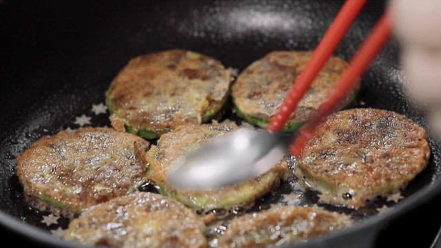 Cooking zucchini pancakes in an oiled frying pan with chopsticks