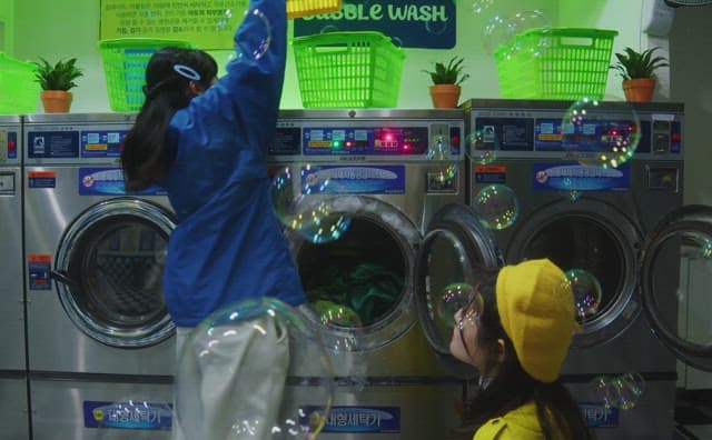 Two women sorting laundry in a laundromat filled with bubbles