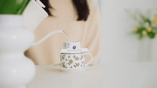 Woman pouring water into cup with coffee pot on table