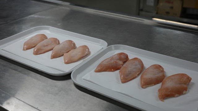 Trays of raw chicken breasts on a metal counter in a food processing facility