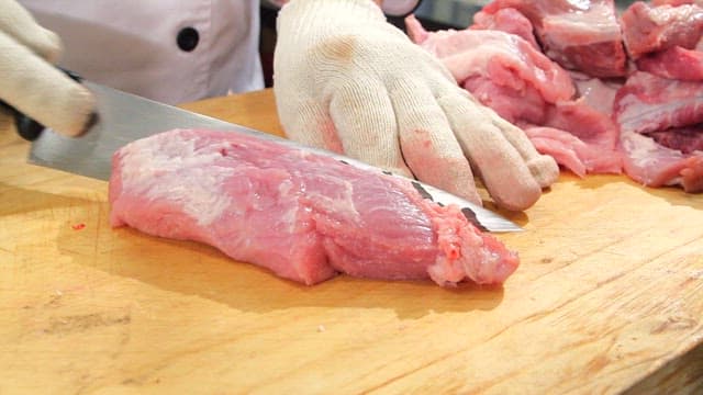 Slicing raw pork on a wooden cutting board with knife