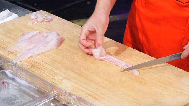 Slicing trimmed flatfish on a wooden cutting board