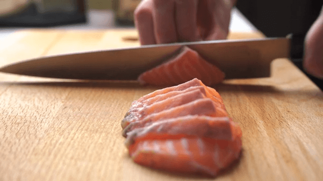 Side view of cutting fresh salmon on wooden cutting board