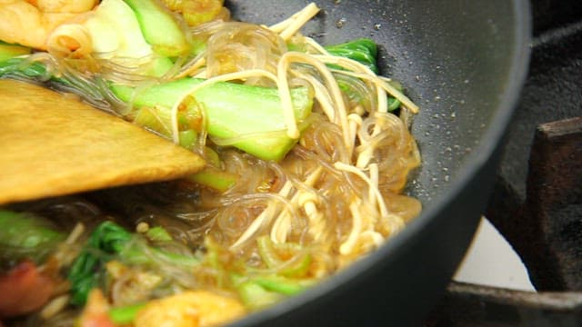 Stir-frying bok choy, noodles, and shrimp in a pan