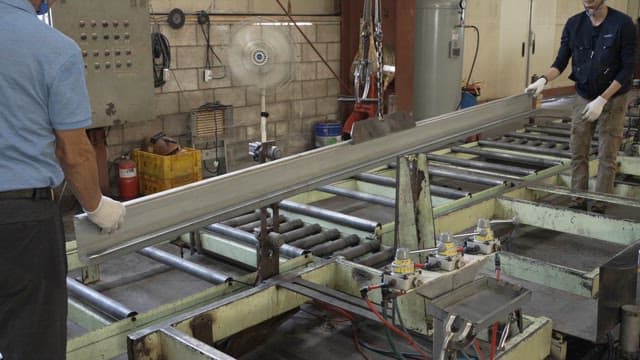 Workers handling metal beams in a factory