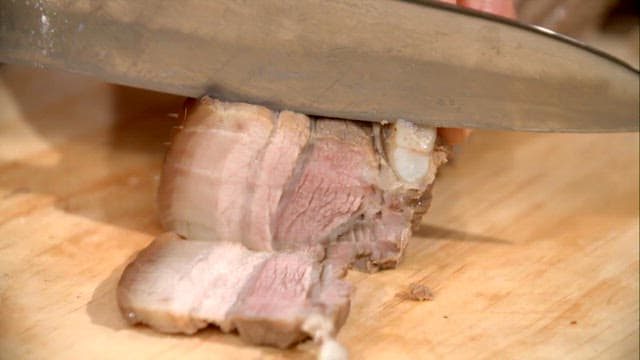 Slicing boiled pork slices on a wooden board