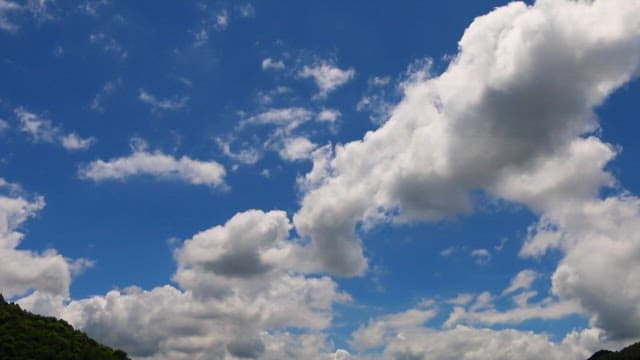 Clouds drifting in a blue sky over lush green mountains