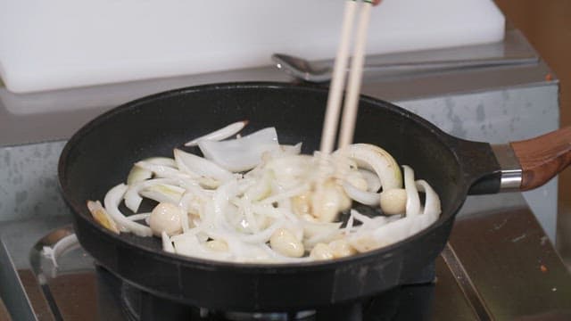 Stir-frying onions with chopsticks in a frying pan