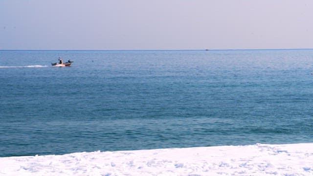 Small motorboat navigating the open sea near the snowy coastline