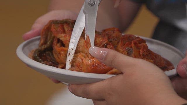 Kimchi being cut with scissors on a plate
