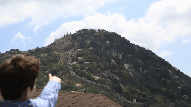 Person pointing with his finger at a mountain landscape with a castle wall and houses