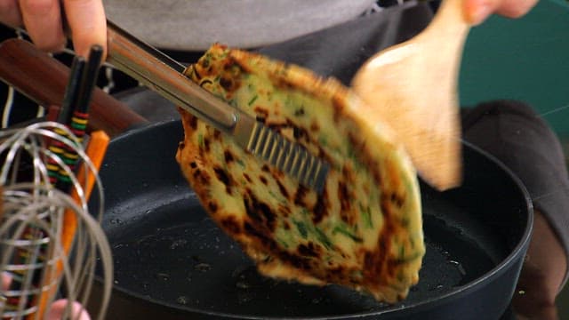 Korean green onion pancake being flipped in a pan
