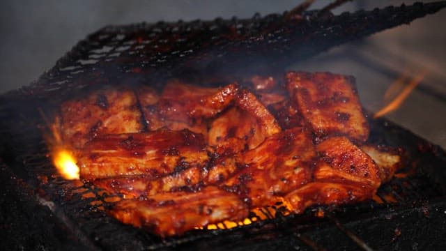 Meat sizzling on a grill over blazing charcoal