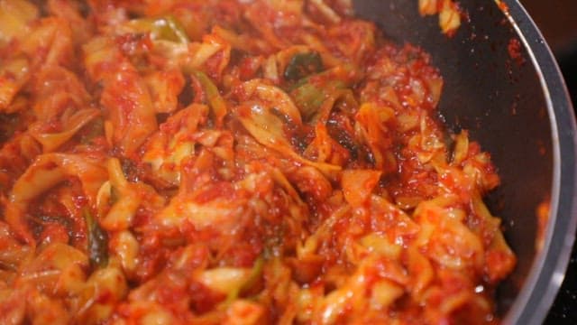 Making spicy stir-fried cabbage in a frying pan with a wooden spatula